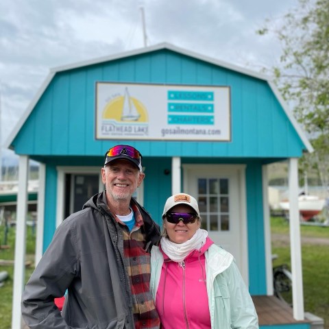 Two people smiling in front of a blue building with a sign about lessons and rentals.