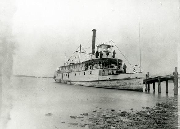 Black and white photo of a vintage steamship docked at a pier with people on deck.