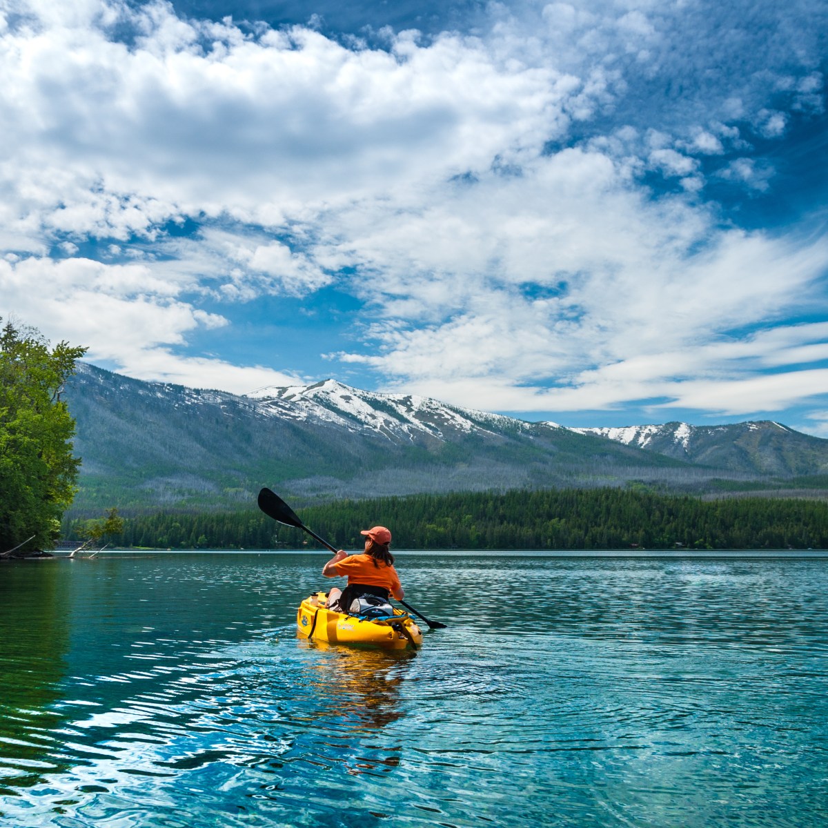 Person kayaking on a lake with mountains and trees in the background.