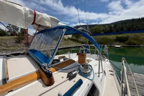 Sailboat docked with blue canopy, coiled ropes, and lush greenery in the background.